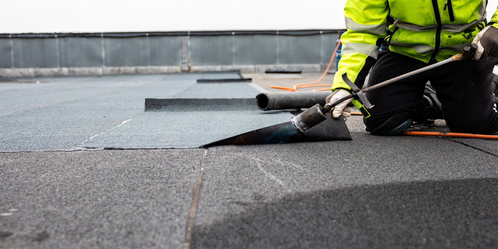 professional roofer applying bitumen roll on flat roof with a gas burner at a modern construction site